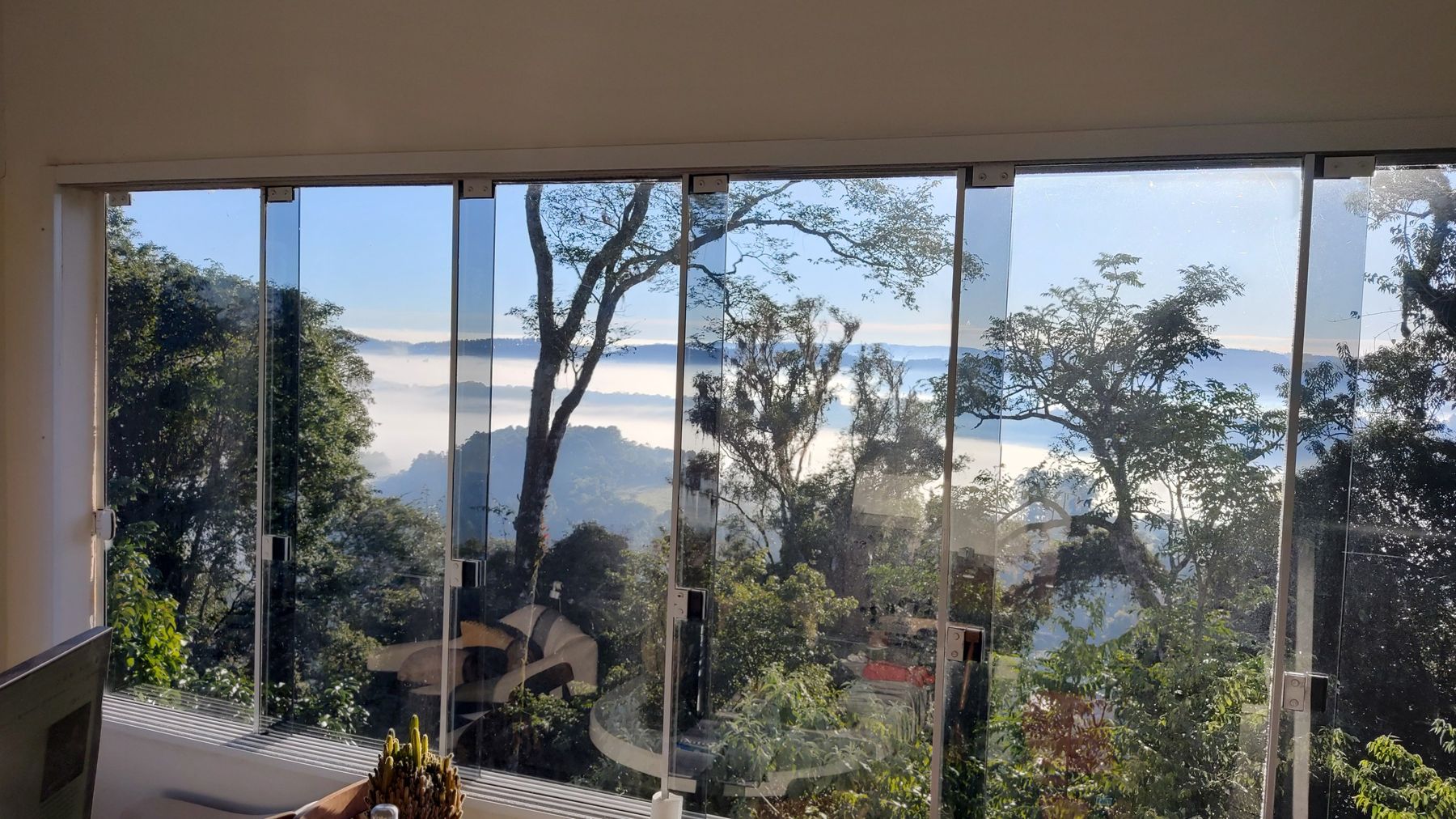 Vista do janelão da casa para o vale coberto de neblina ao amanhecer